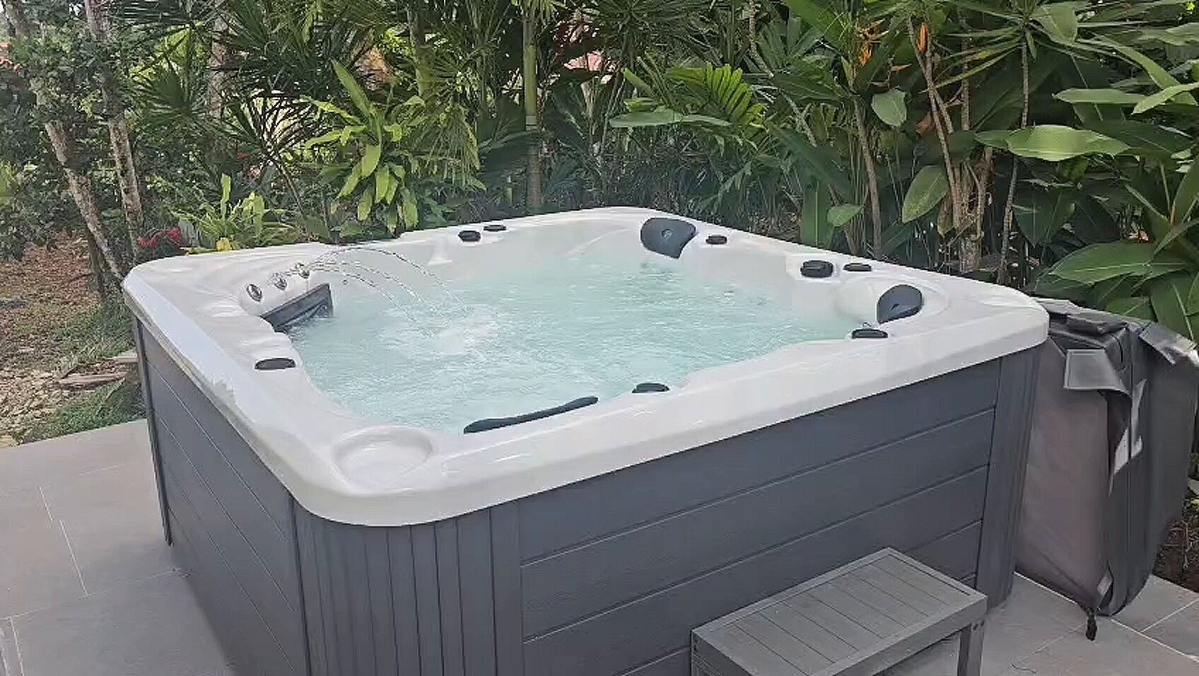 A hot tub with a built-in seat, surrounded by lush greenery.