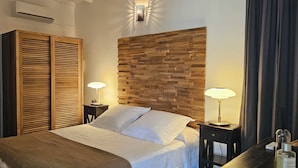 Habitació d'hotel amb un llit, un panell de capçalera de fusta, dues làmpades de nit, un armari i una taula petita amb una làmpada i una ampolla.