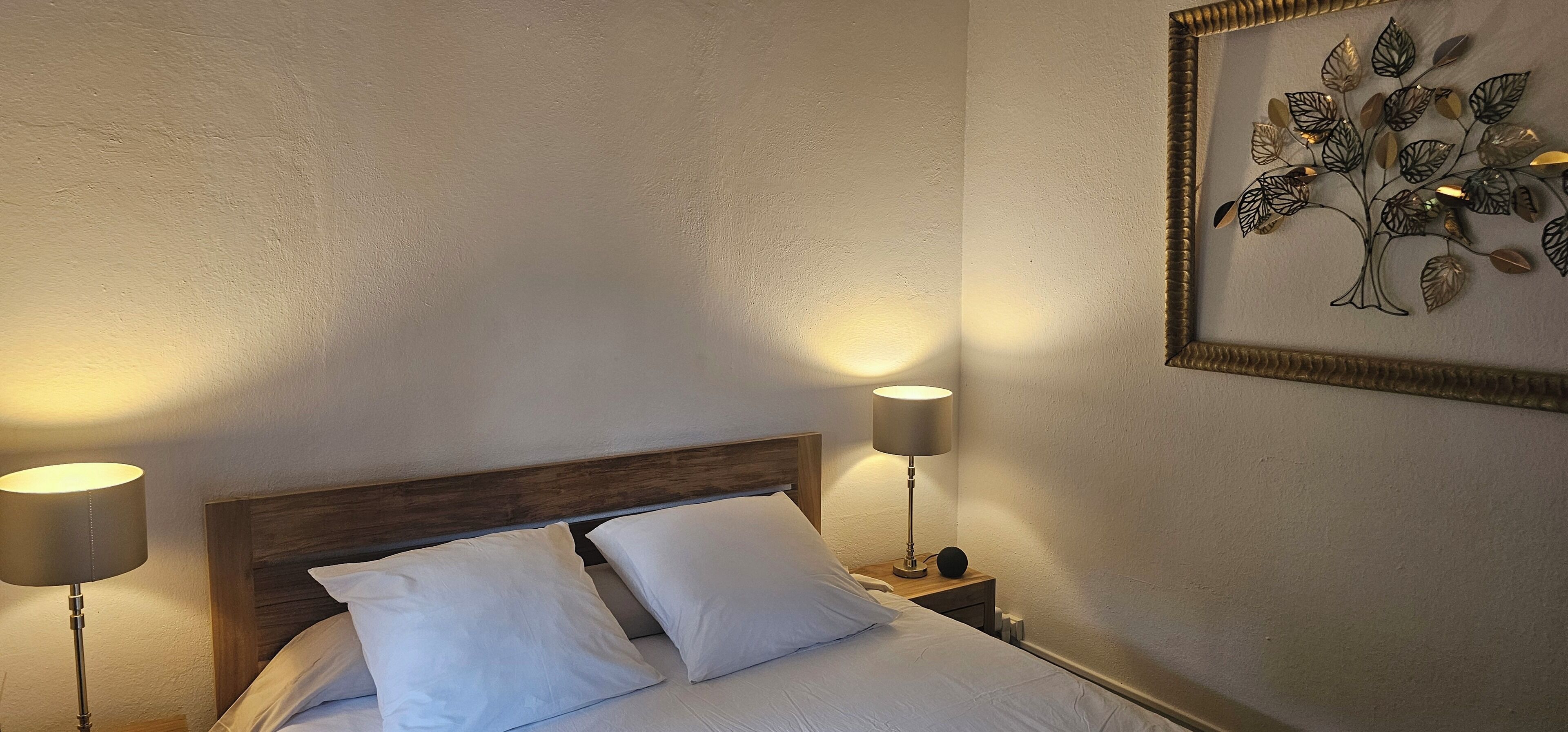 Un lit bien fait, avec du linge de lit blanc et deux lampes de chevet.