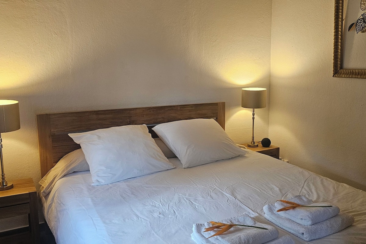 A neatly made bed with white linens and two pillows, flanked by two bedside lamps on wooden nightstands.