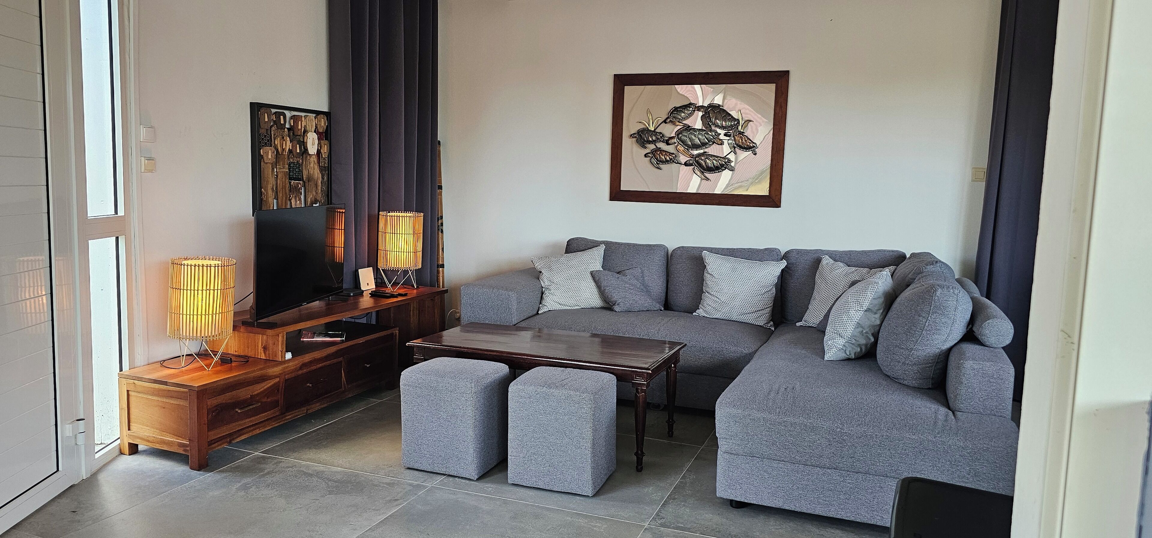 A modern living room with a grey sofa, ottomans, a wooden coffee table, a TV, and a floor lamp.