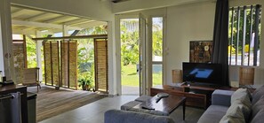 Amplia sala de estar con televisión, sofá y vistas a un jardín exuberante a través de puertas abiertas.