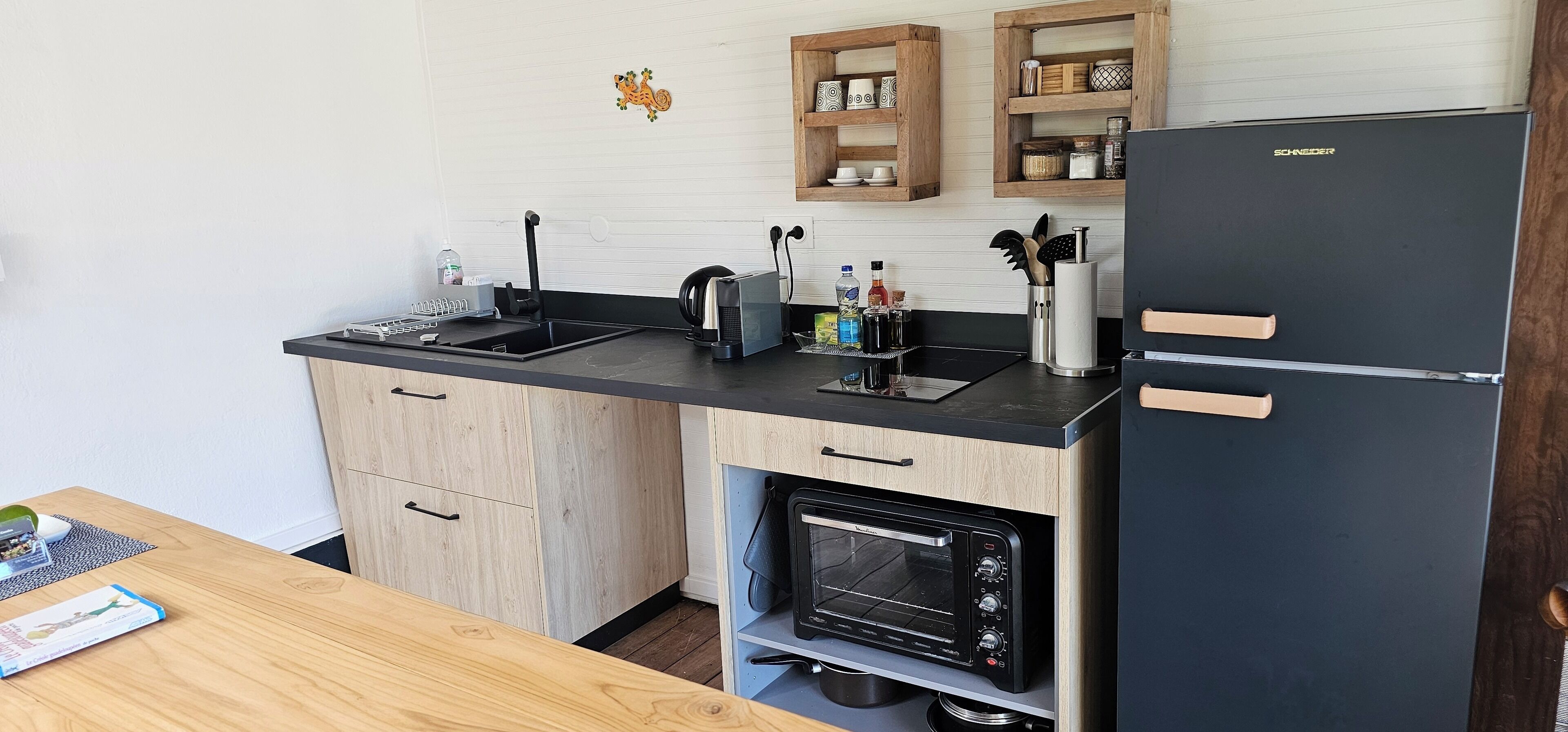 Een kleine keuken met een zwarte koelkast, een inbouwoven, een spoelbak en houten keukenkastjes.