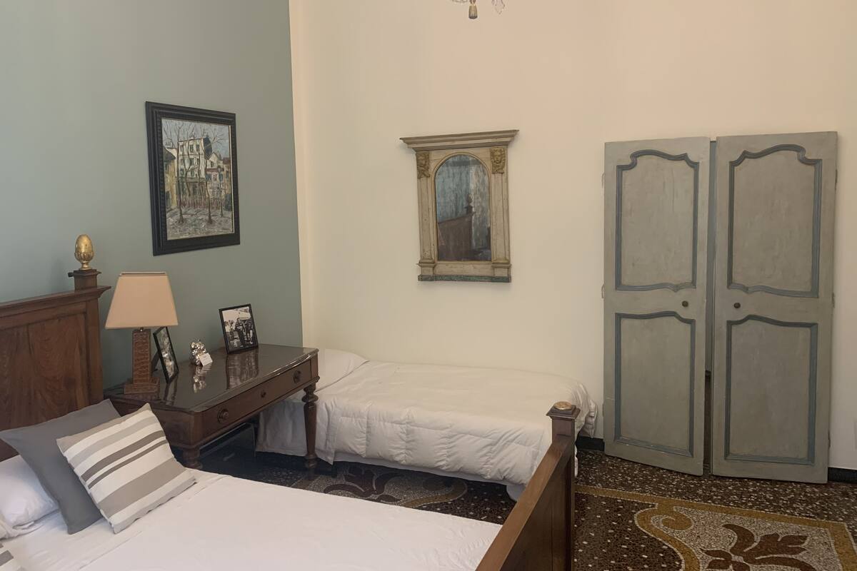 A bedroom with two beds, a wooden dresser, a chandelier, a framed picture, and a mirror.