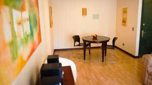Una habitación con una mesa redonda, dos sillas, un cuadro pequeño en la pared y una puerta.