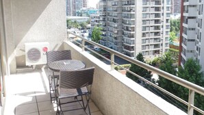 Un balcón con dos sillas de mimbre y una mesita pequeña, con vistas a un paisaje urbano con edificios altos.
