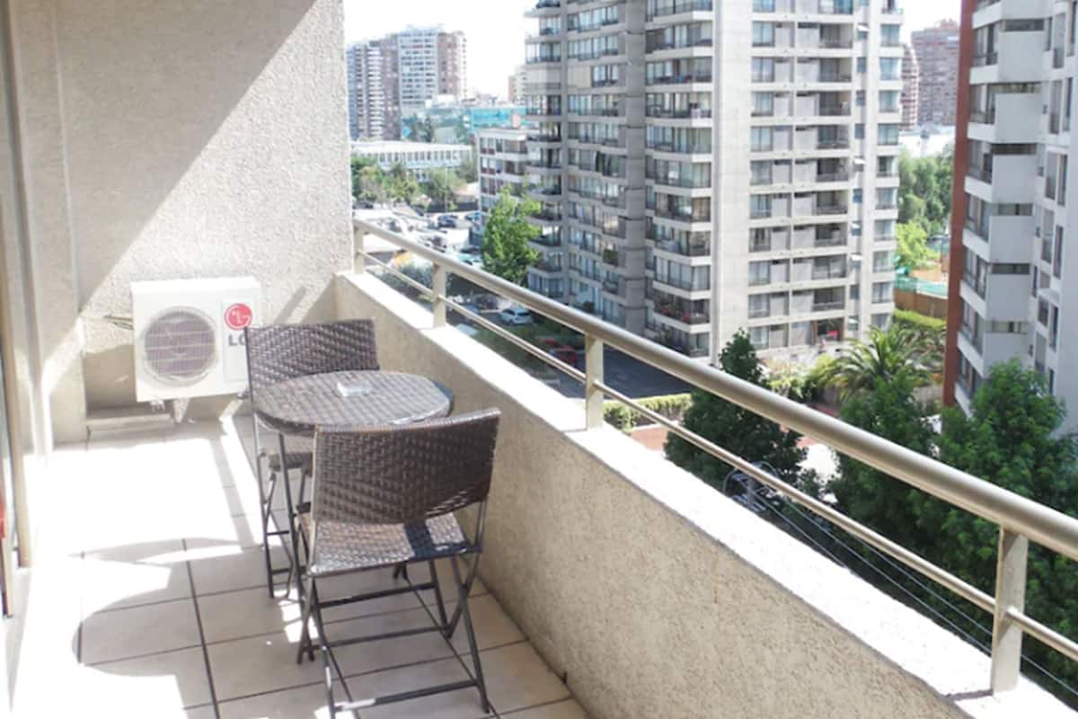 Ein Balkon mit zwei Korbstühlen und einem kleinen Tisch mit Blick auf eine Skyline aus hohen Gebäuden.