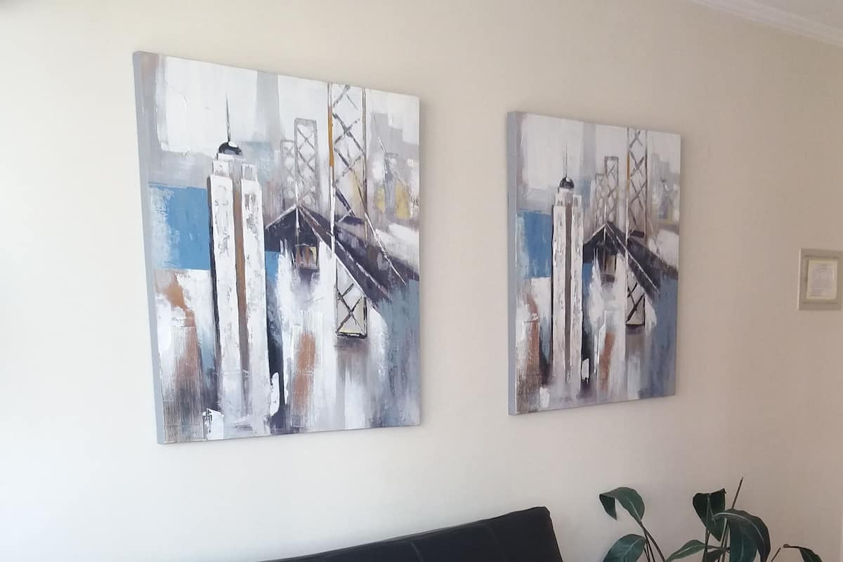 Ein schwarzes Sofa mit roten Kissen, zwei abstrakte Gemälde an der Wand, eine Topfpflanze und ein Glastisch mit einer Fernbedienung.