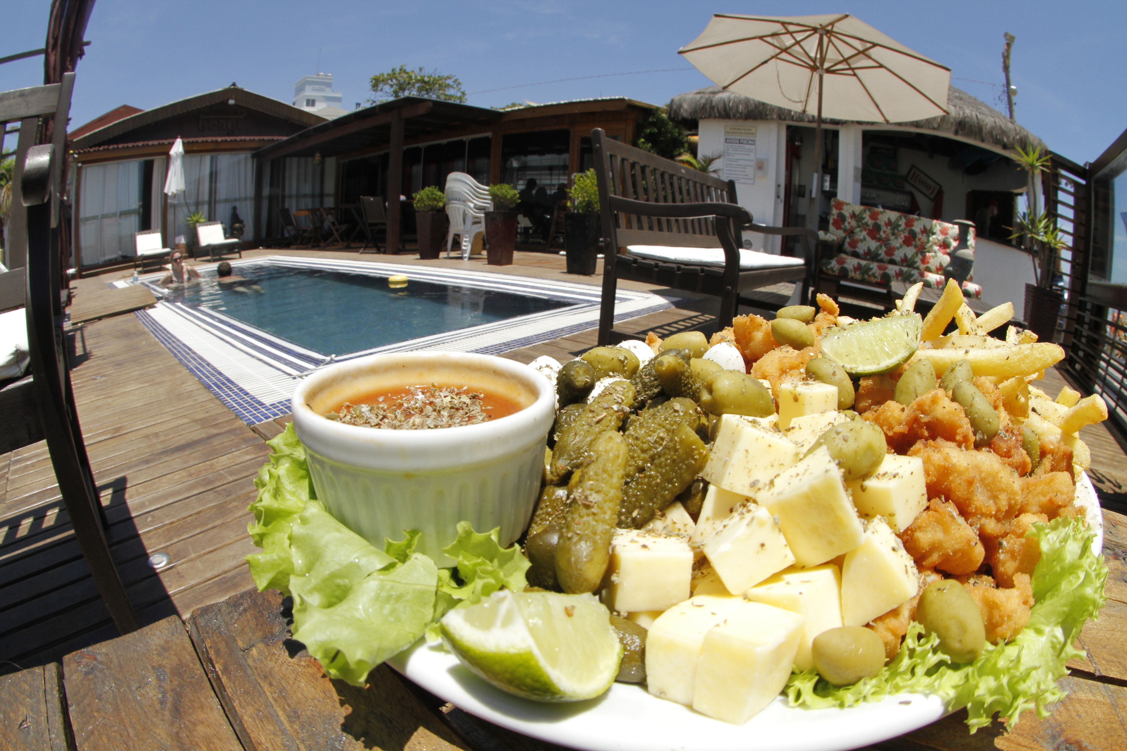Un espace repas aménagé au bord de la piscine, avec une assiette de nourriture comprenant du fromage, des olives et un quartier de citron vert.