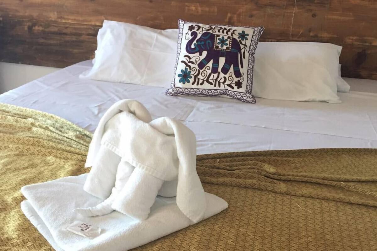 Un llit ben arropat amb un estenat estampat, un coixí decoratiu amb un disseny d'elefant, i una tovallola doblegada al llit.