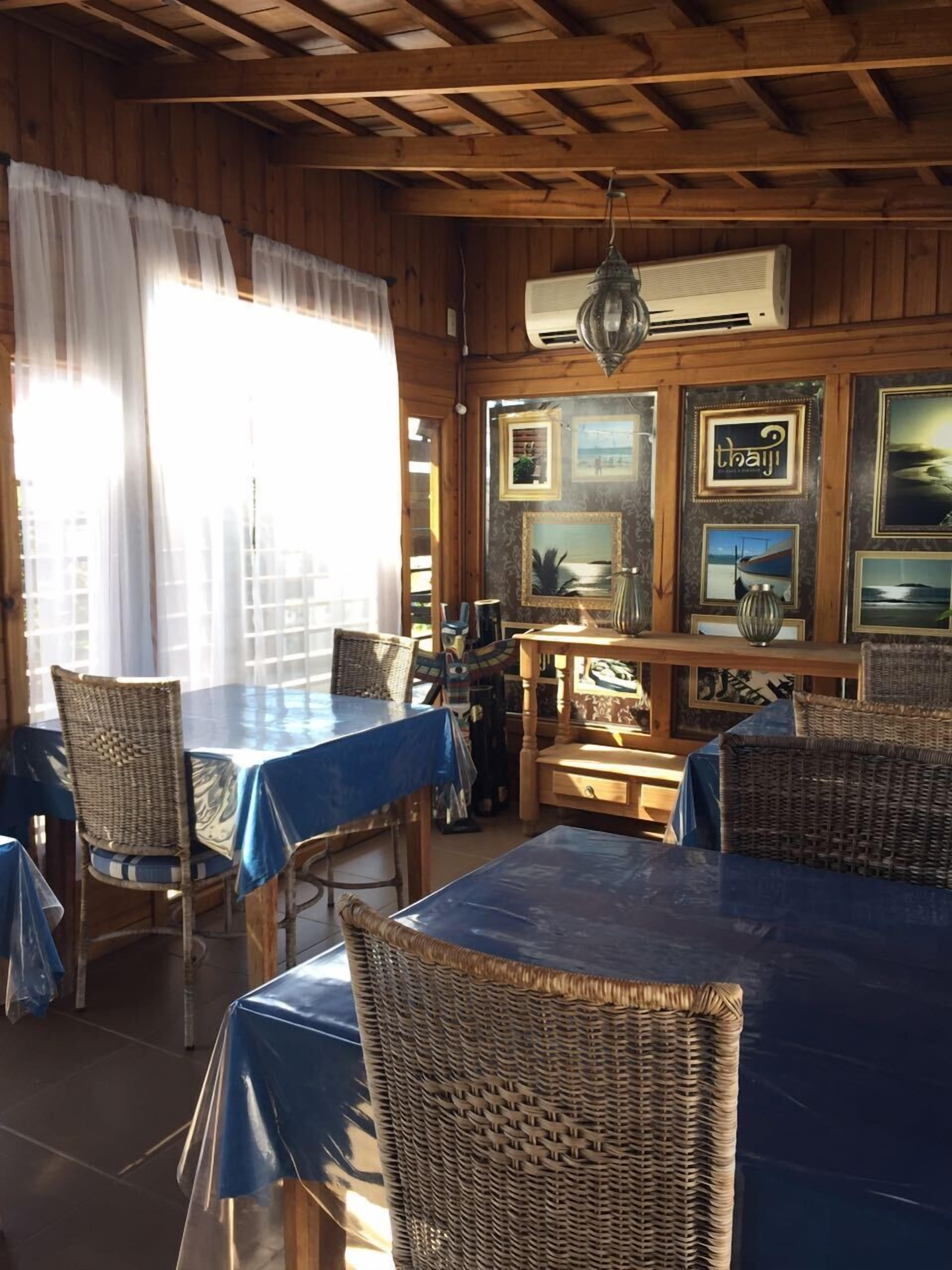 Een houten interieur met tafels met blauwe tafelkleden, rieten stoelen en ingelijste foto's aan de muren.