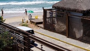 A beach with a thatched-roof hut, a paved walkway, and a view of the sea. - Thaiji Pousada e Parador (Florianópolis)