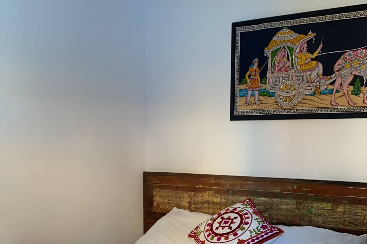 Un llit amb roba blanca, un llençol vermell estampat i un coixí decoratiu.