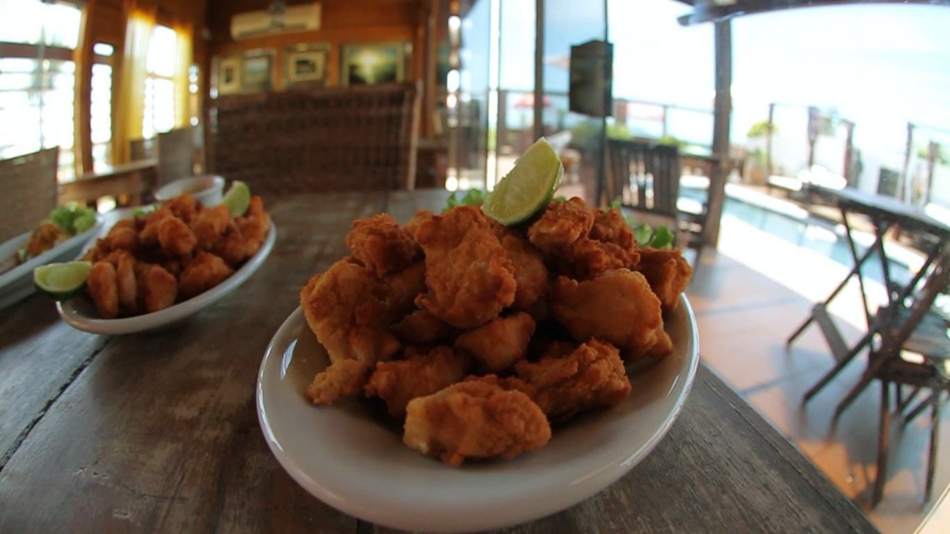 A restaurant with a wooden table displaying plates of fried food and a view of the ocean.