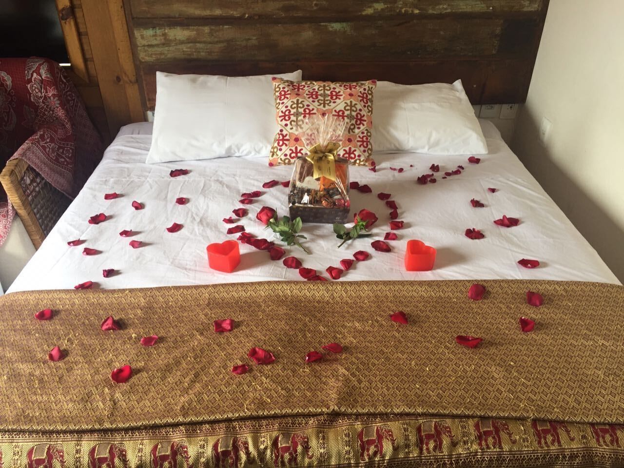 A bed with rose petals and a heart-shaped arrangement of red rose petals.
