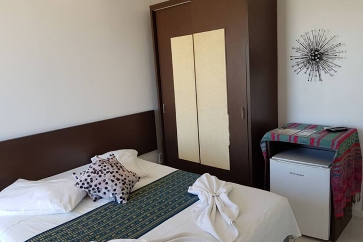 Habitació d'hotel amb llit, armari, nevera petita i una decoració mural.