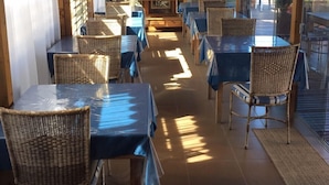 A restaurant with wooden ceiling beams, wicker chairs, and tables covered with blue tablecloths. - Thaiji Pousada e Parador (Florianópolis)