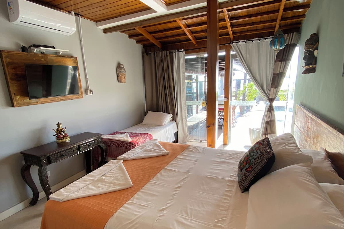 Habitació d'hotel amb sostre de fusta, un llit gran amb roba de llit blanca i taronja, una taula petita amb una estàtua, i una finestra amb cortines.