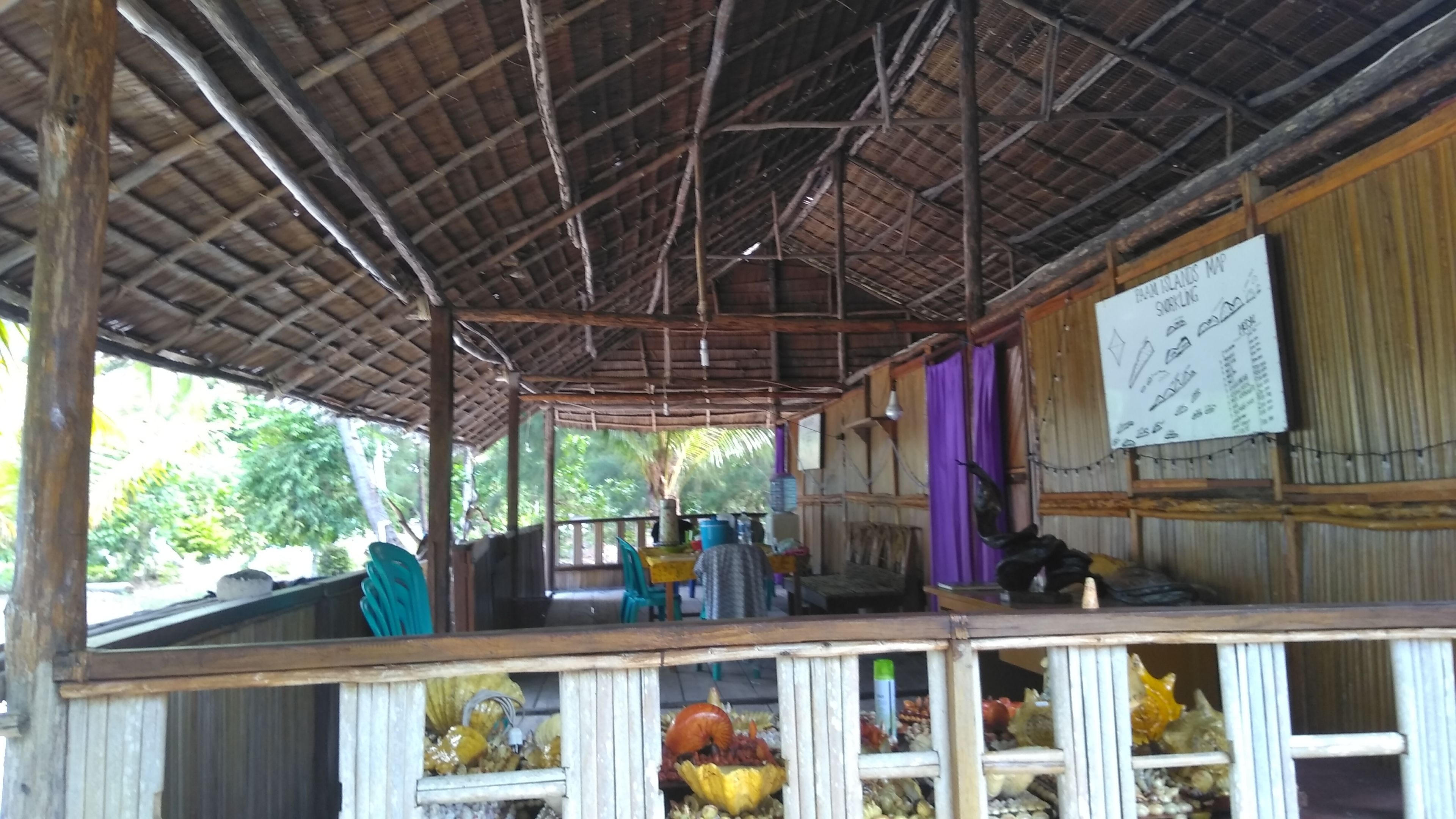 A rustic wooden structure with a thatched roof, a covered seating area, and a signboard.