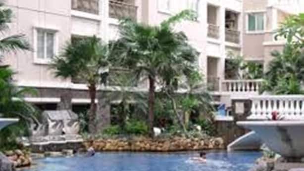 A swimming pool with palm trees and a fountain, surrounded by a building with balconies. - Sudirman Park Apartment by Merry (Jakarta)