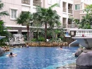 Una piscina con palmeras y una fuente, rodeada por un edificio con balcones.