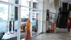 A spacious lobby with large glass doors leading outside, a staircase, and a cart with items. - Sudirman Park Apartment by Merry (Jakarta)