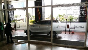A car parked inside a building with a glass door, a tiled floor, and a sign with text in a foreign language. - Sudirman Park Apartment by Merry (Jakarta)