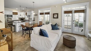 A spacious living area with a white sofa, a dining table, and a kitchen in the background.