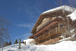 A multi-story wooden chalet with balconies, surrounded by snow.