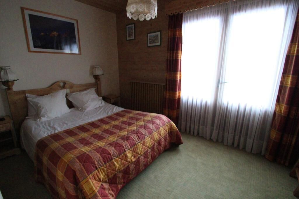 Une chambre à coucher avec une tête de lit en bois, une couvre-lit matelassé, deux lampes de chevet, un radiateur et une fenêtre avec des rideaux.