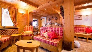L’intérieur d’un chalet en bois chaleureux et accueillant, avec un canapé, des fauteuils, une table ronde et une cheminée.