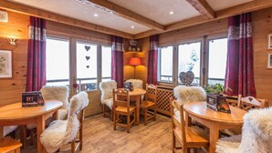 Un intérieur chaleureux en bois, avec des tables et des chaises rondes, une lampe centrale et des décorations en forme de cœur sur les fenêtres.