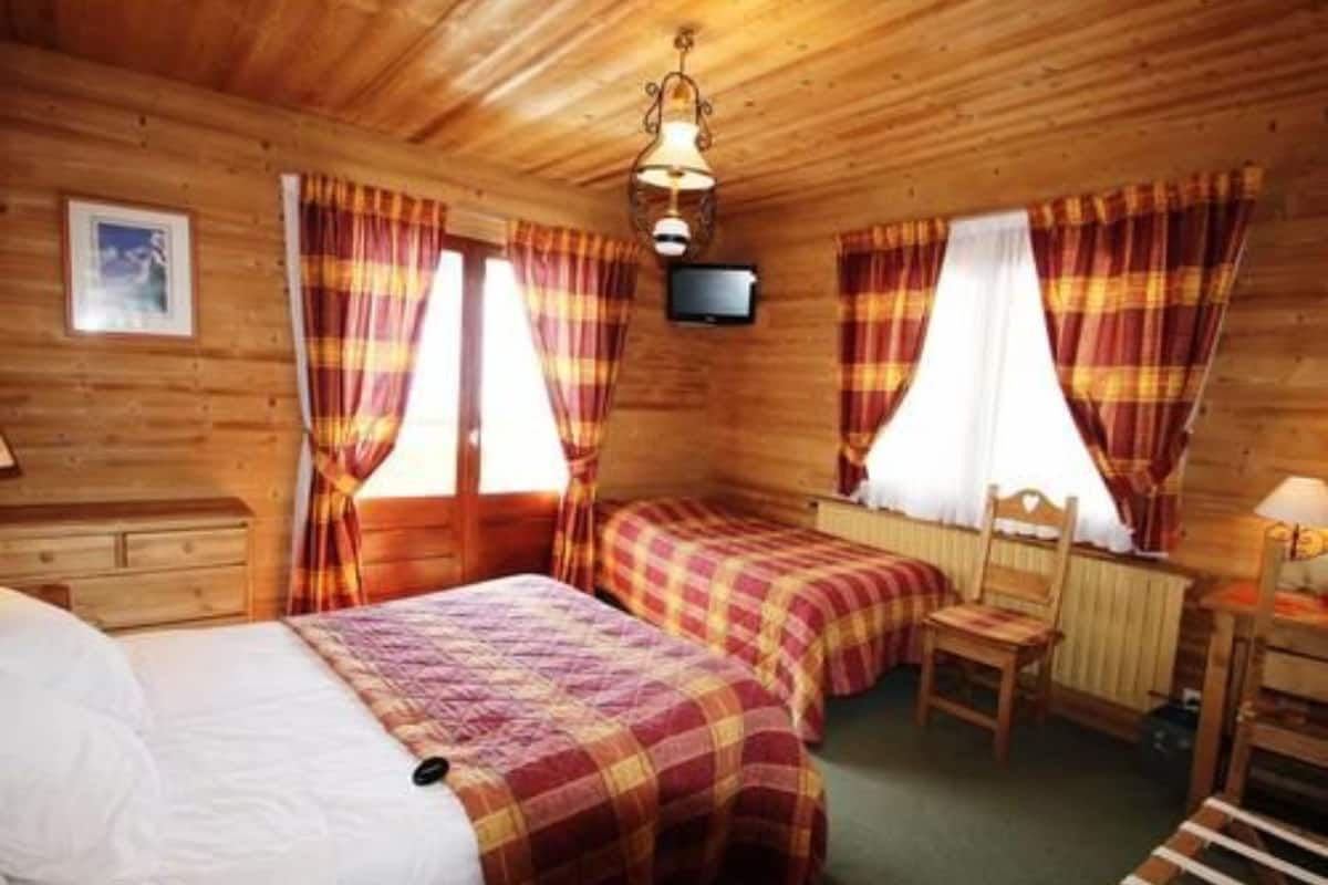 Une chambre de style cabane en bois, équipée de deux lits, d’une télévision et d’une fenêtre avec des rideaux.
