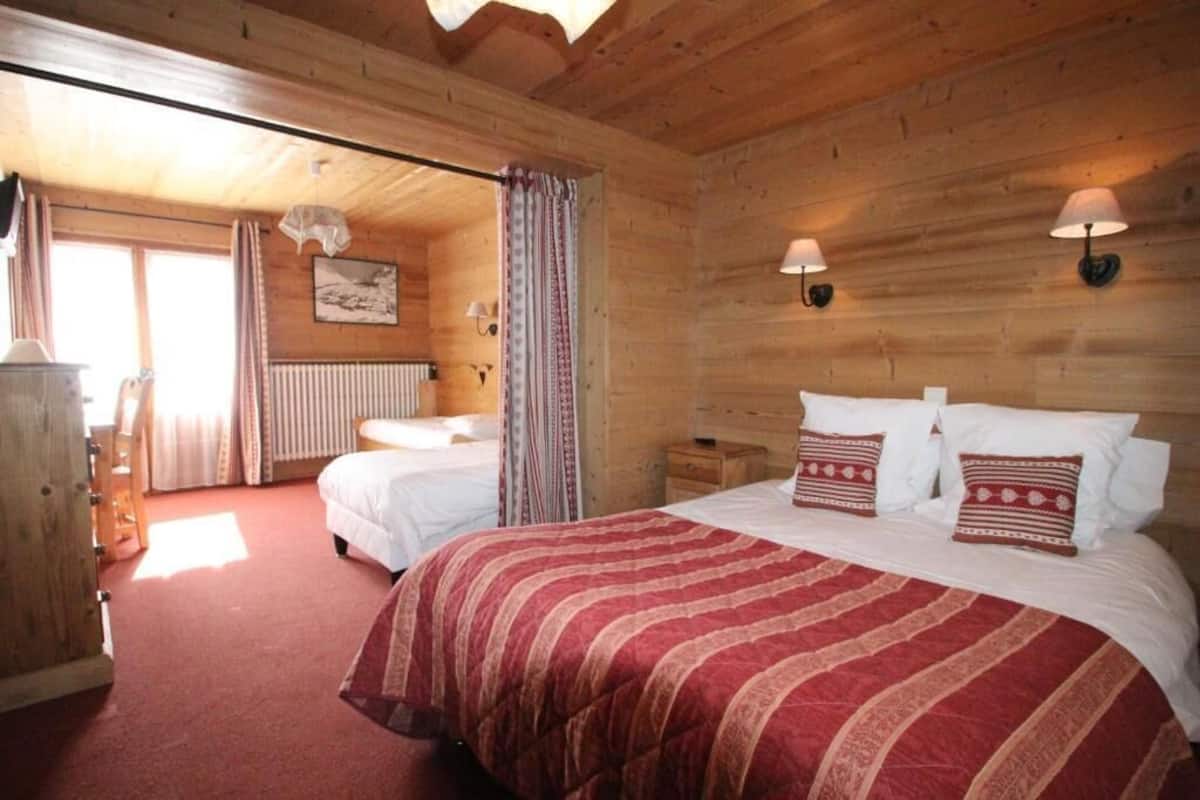 Une chambre dans un chalet en bois, avec deux lits, un radiateur et des lampes fixées au mur.