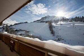 Une piste de ski enneigée, avec un télésiège, une montagne en arrière-plan et un bâtiment en bois doté d’un balcon.