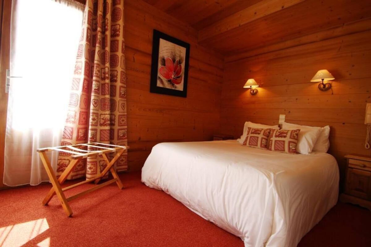 Une pièce en bois avec un lit, un étendoir, des rideaux à motifs et des lampes fixées au mur.