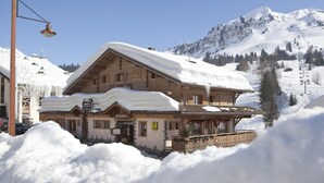 Un bâtiment de style chalet en bois, doté d’un toit en pente, entouré de neige, avec un télésiège visible au loin.