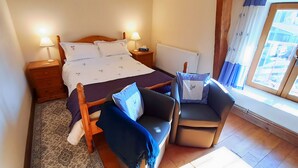 A bedroom with a bed, two bedside tables, a nightstand, a chair, a window with curtains, and a radiator.