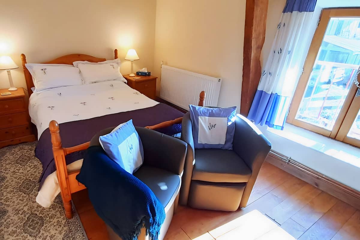 A bedroom with a bed, two bedside tables, a nightstand, a chair, a window with curtains, and a radiator.