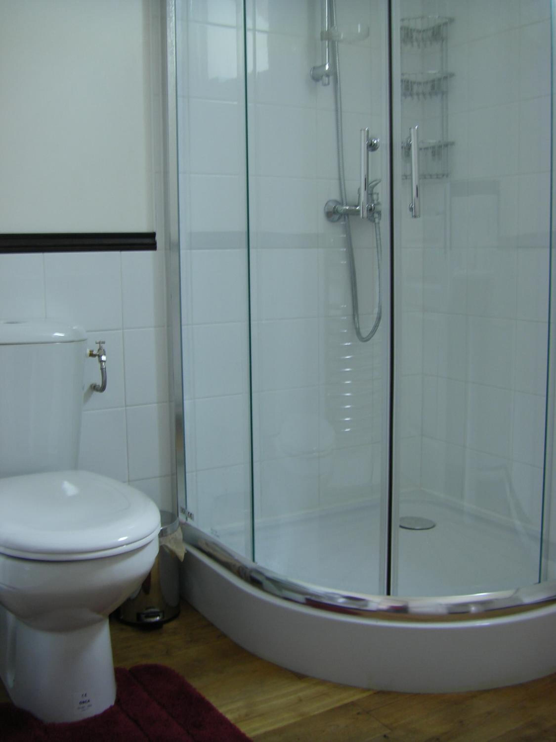 A bathroom with a toilet, a glass-enclosed shower, and a white tiled wall.