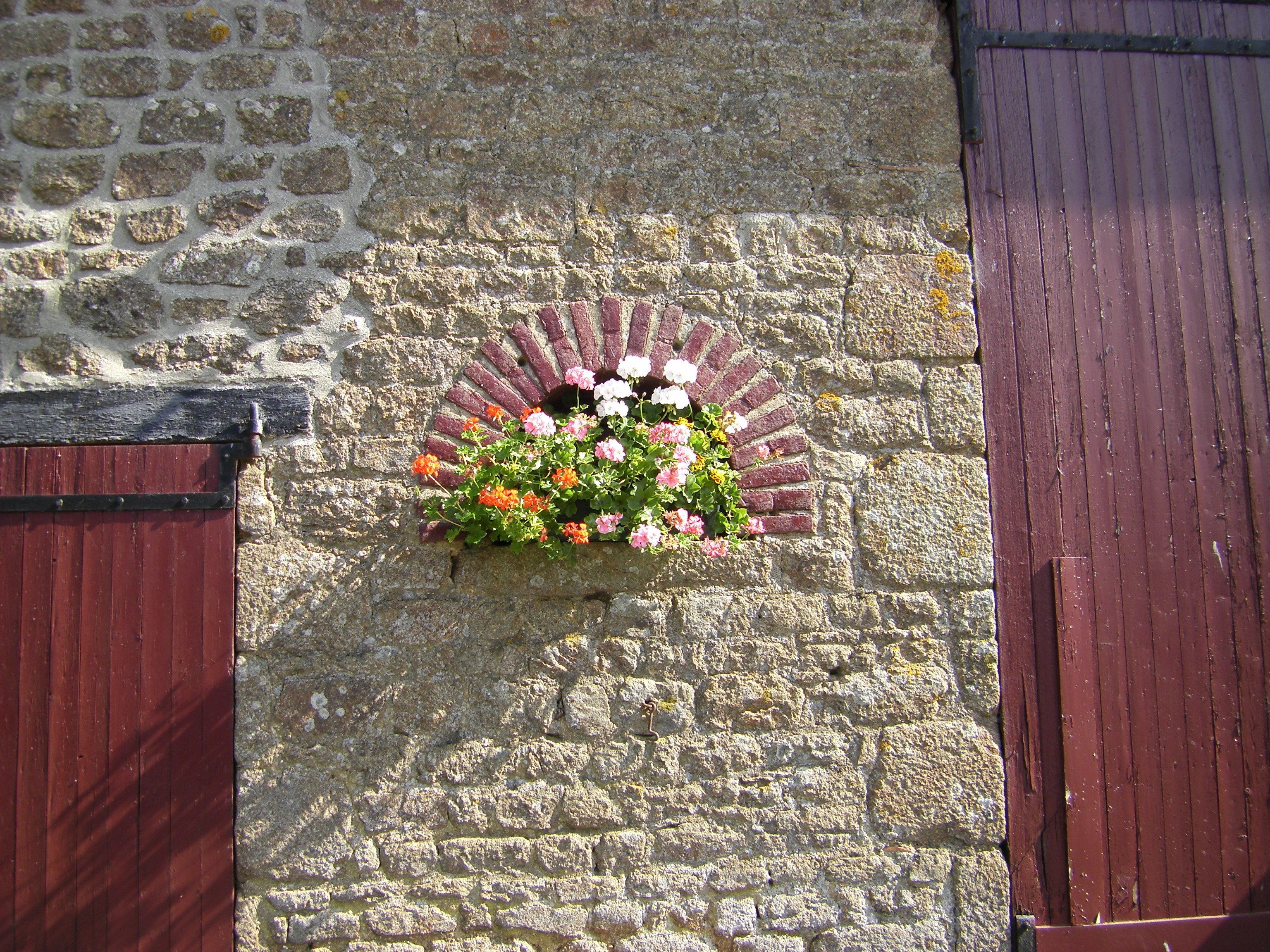 A stone wall with a flower box containing pink, orange, and white flowers.