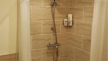 A small, tiled shower area with a handheld showerhead, a shower caddy, and a shower curtain.