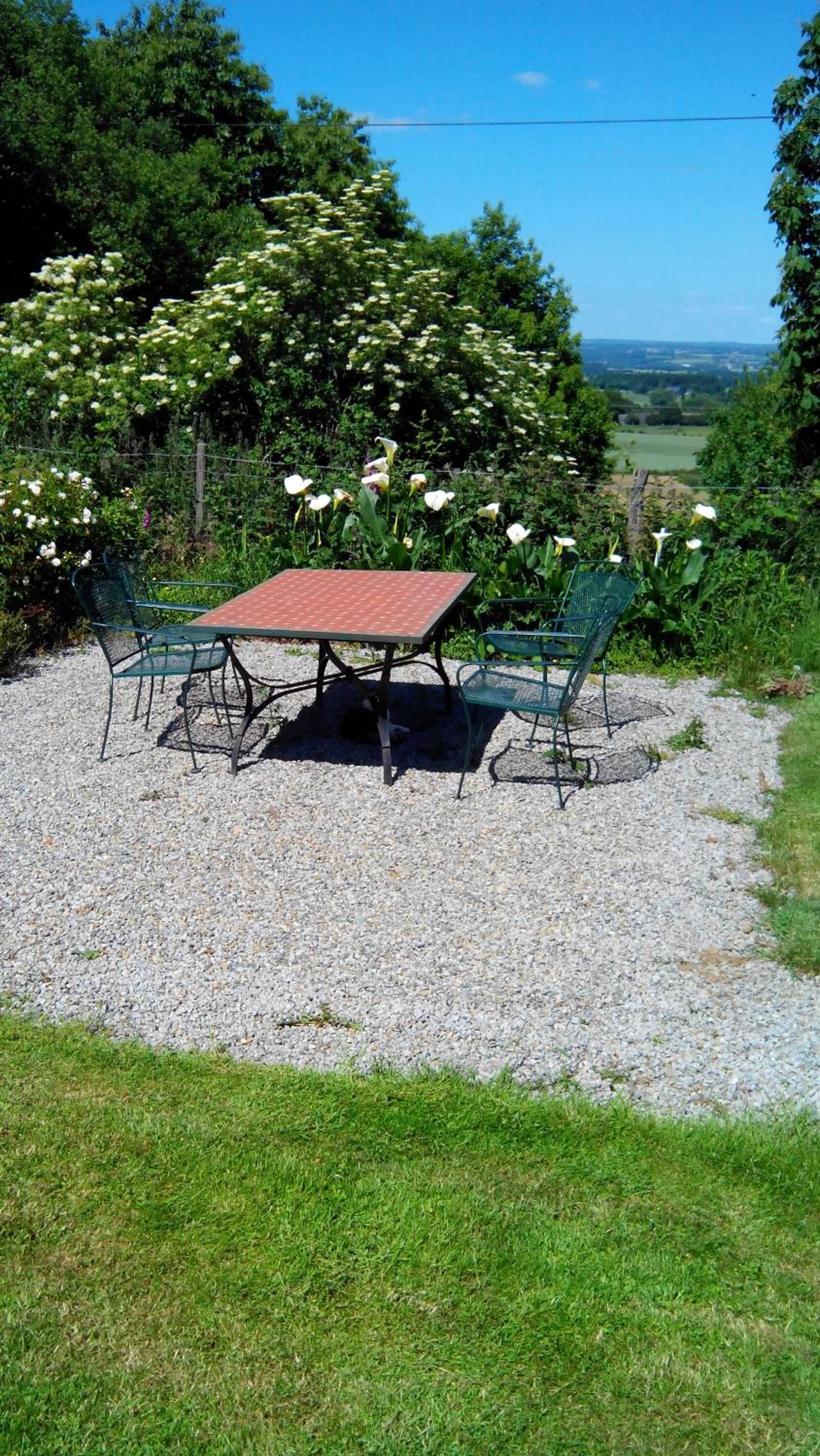 An outdoor seating area with a table and chairs, surrounded by gravel and greenery.
