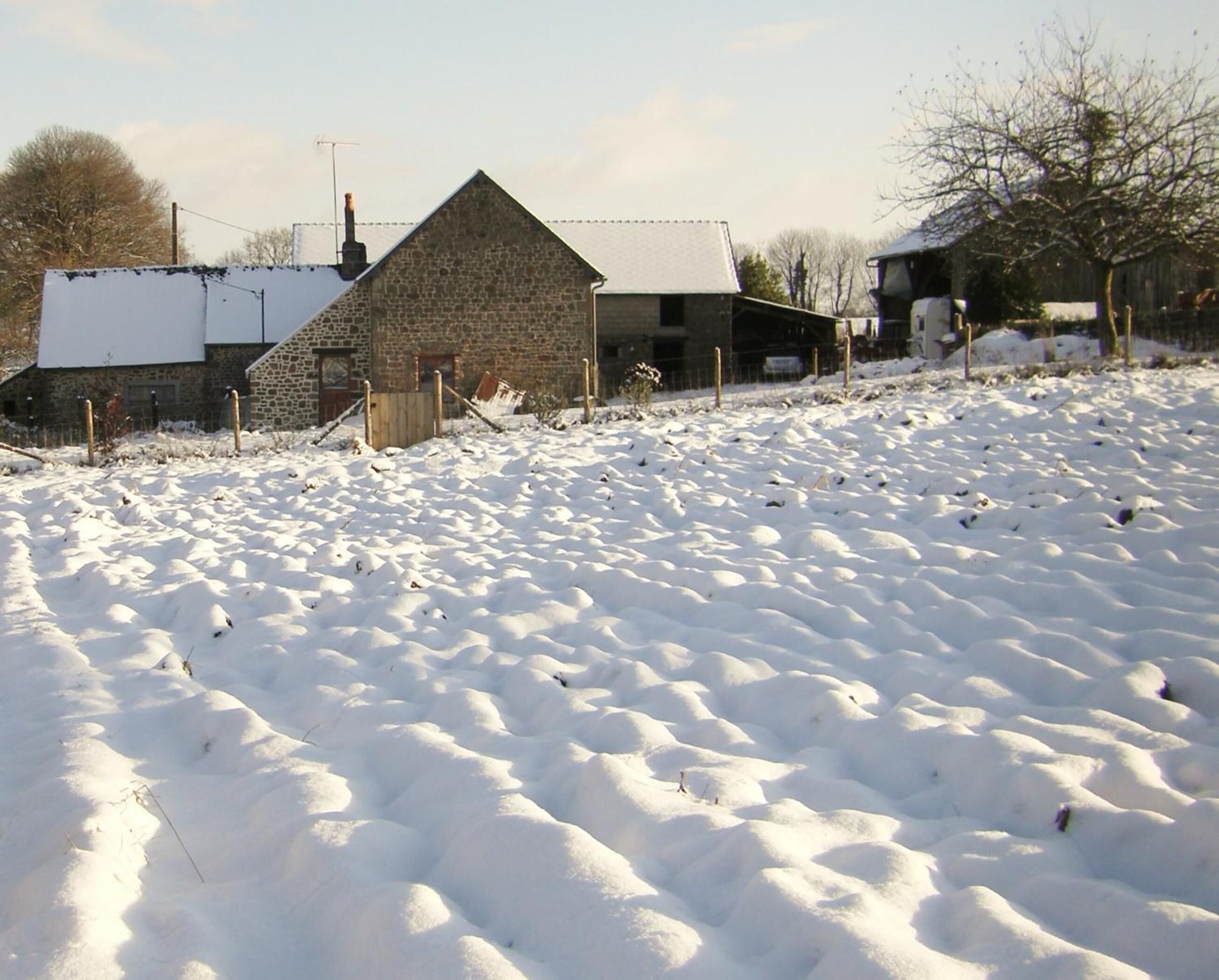 A snow-covered field with a stone building and a wooden fence.