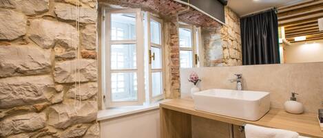 A bathroom with a stone wall, a window, a sink, and a mirror.