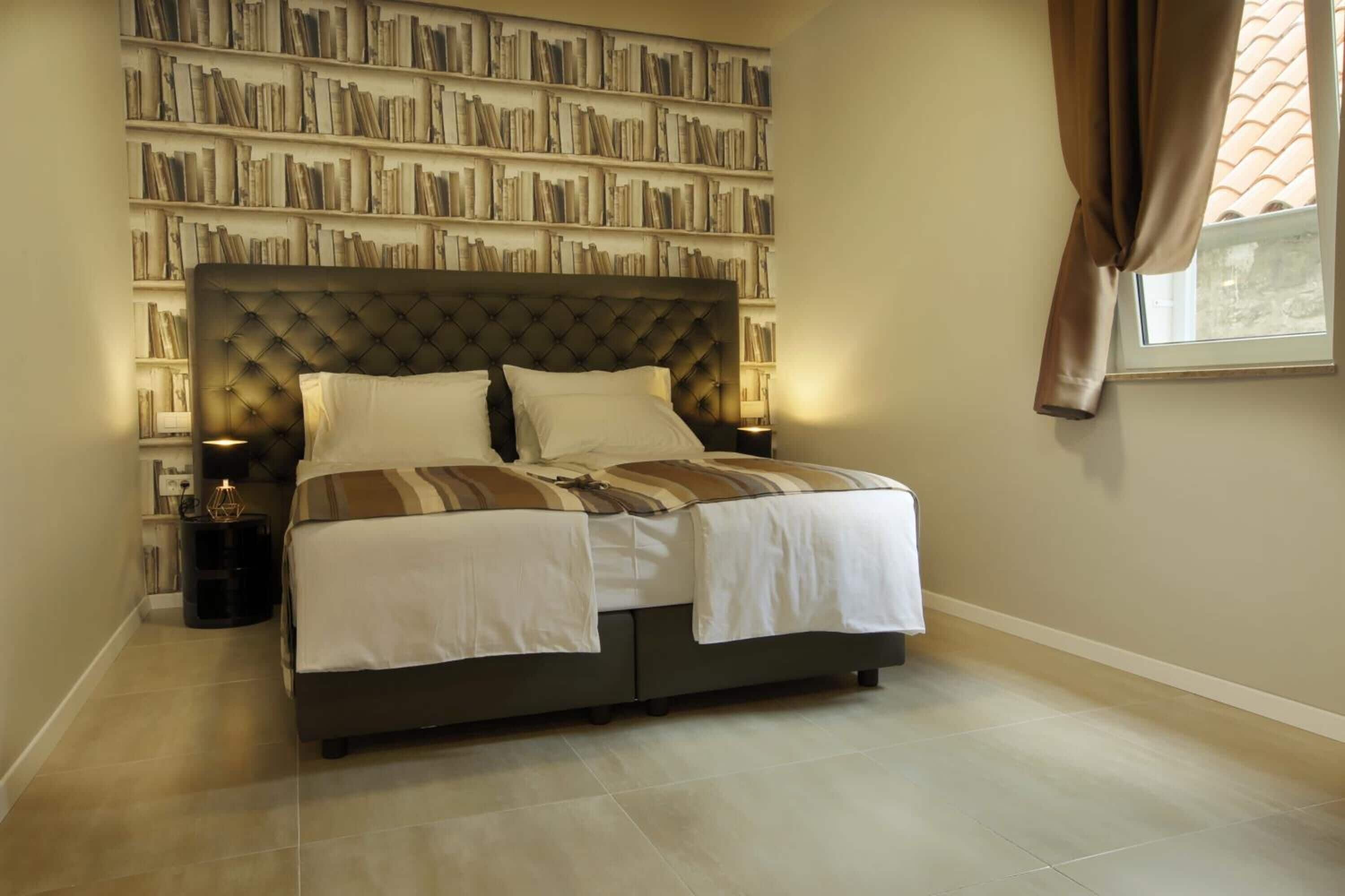 A bedroom with a large bed, a bookshelf wall, and a window with curtains.