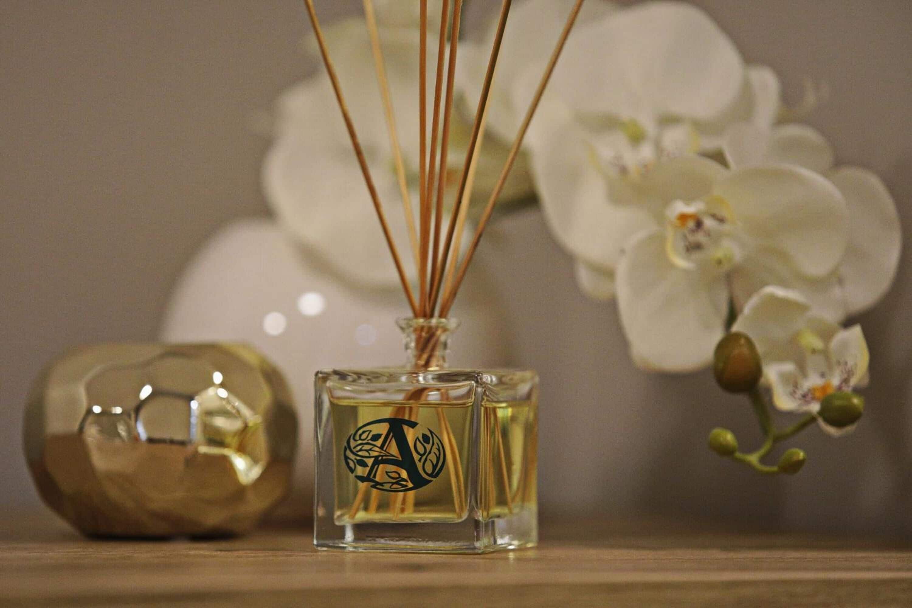 A square bottle with a decorative emblem, a round metallic object, and white flowers in the background.