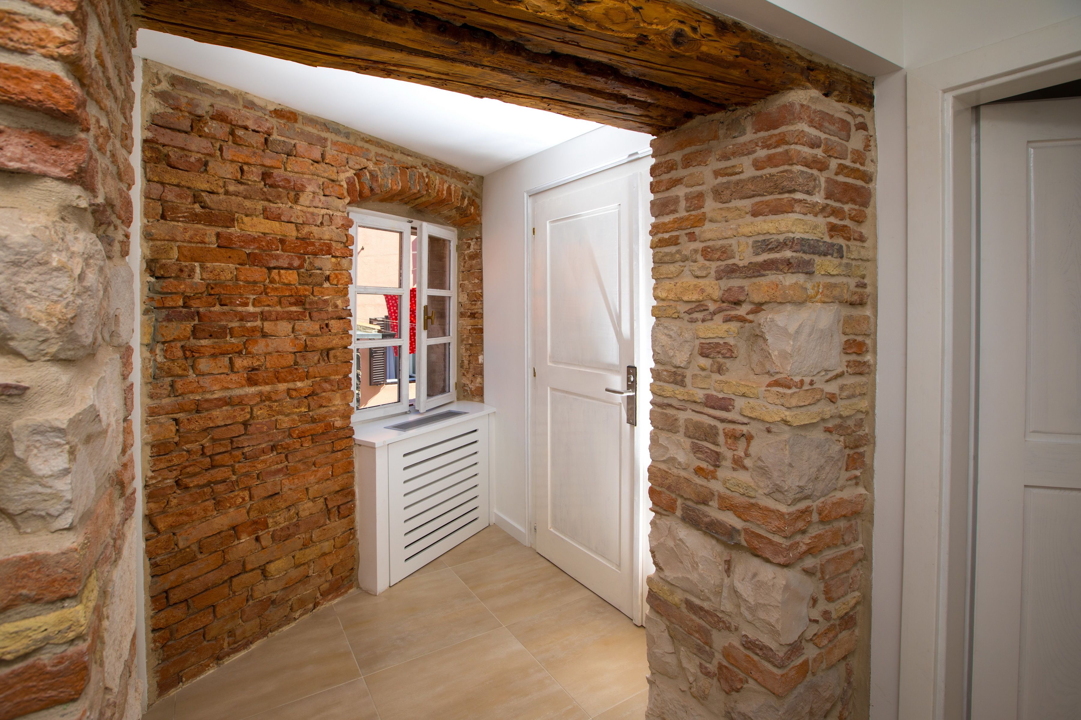 A narrow hallway with exposed brick walls, a white door, and a window with blinds.