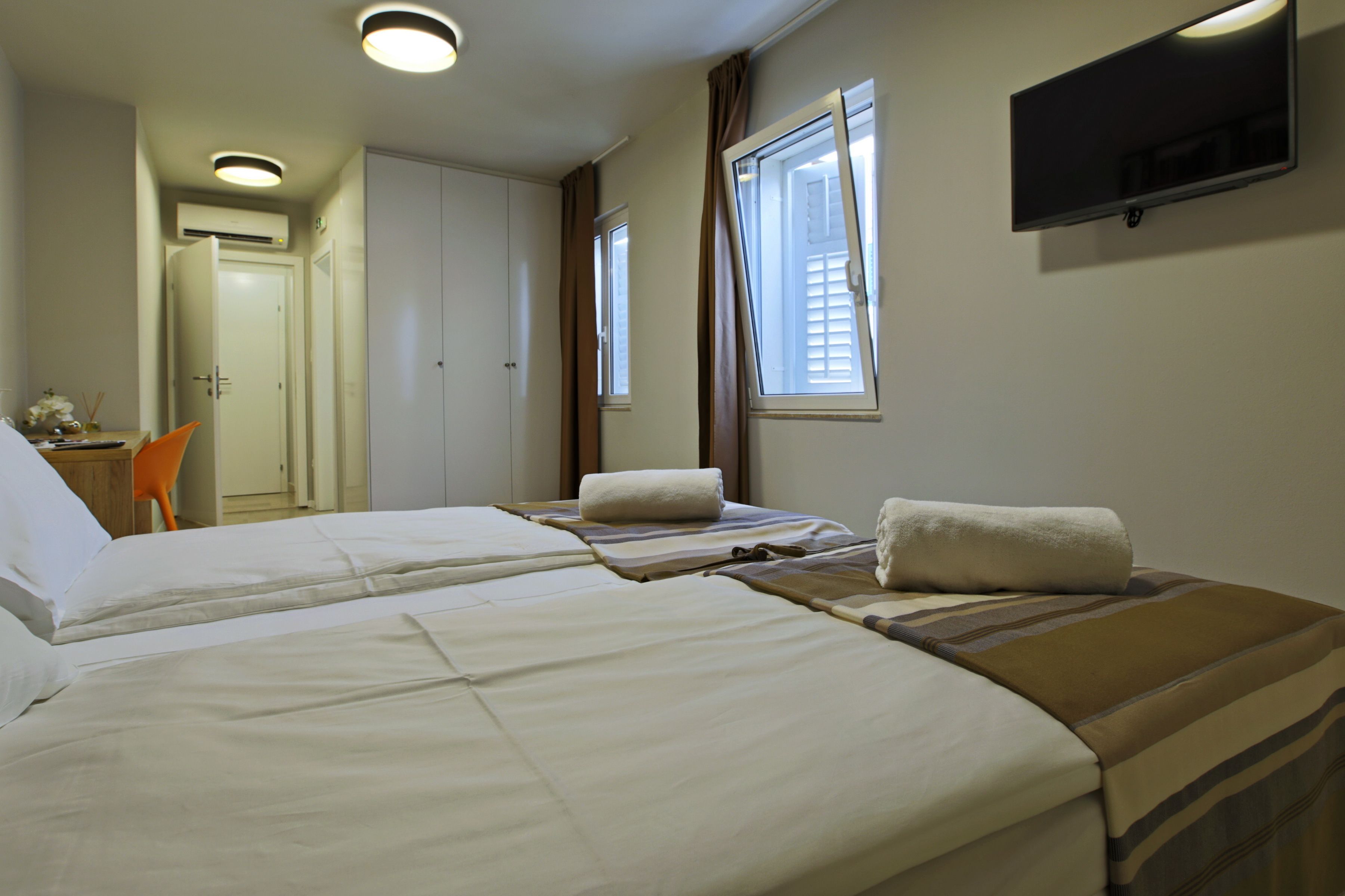 A hotel room with two beds, a TV mounted on the wall, and a small table with a chair.