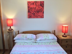 A neatly made bed with floral bedding, two bedside lamps, and a wall art of roses. - One bedroom Wyvis (Inverness)